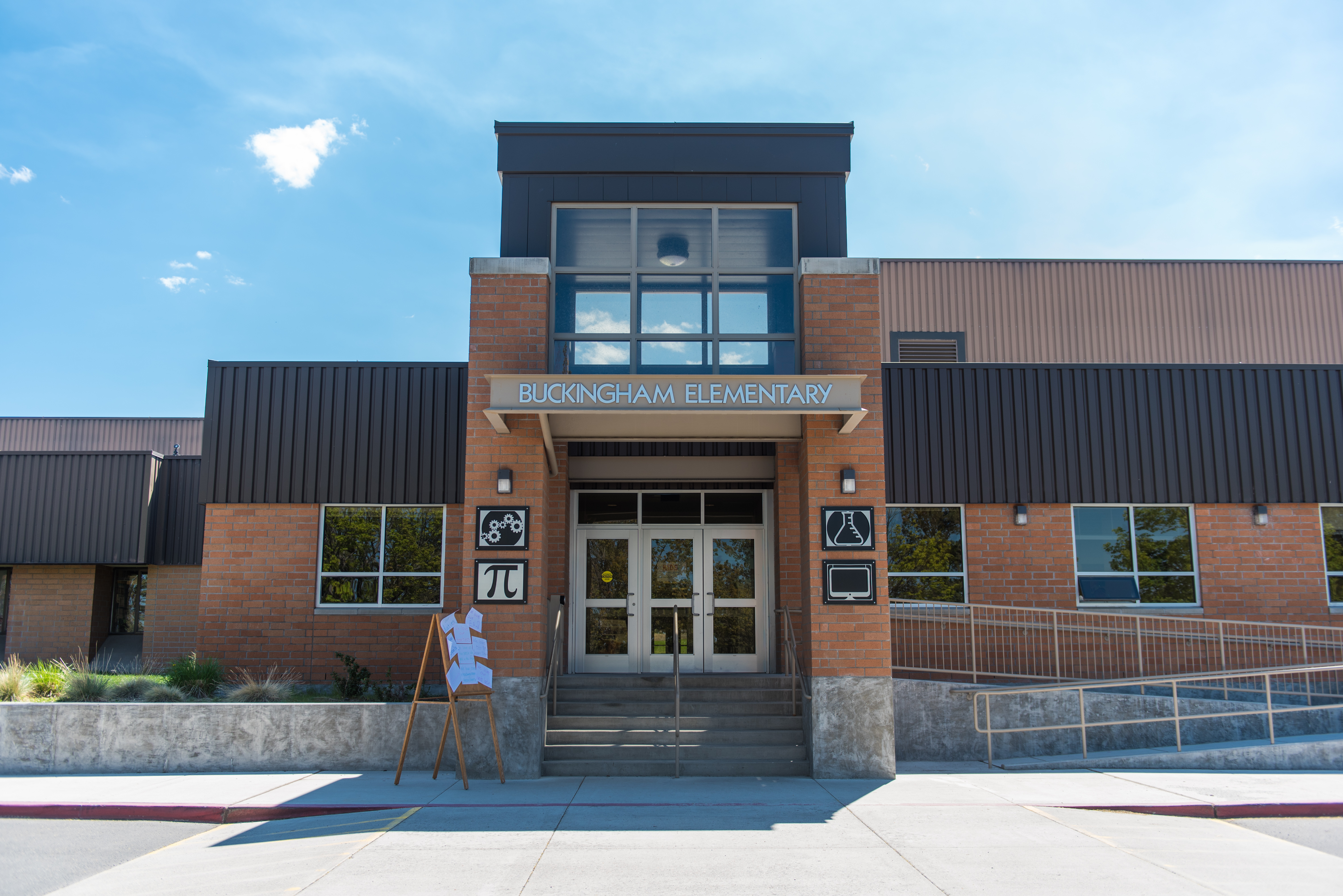 School entrance of single level school with two stories of windows in entryway. Words Buckingham Elementary are over the entrance in silver letters and blue sky is above.