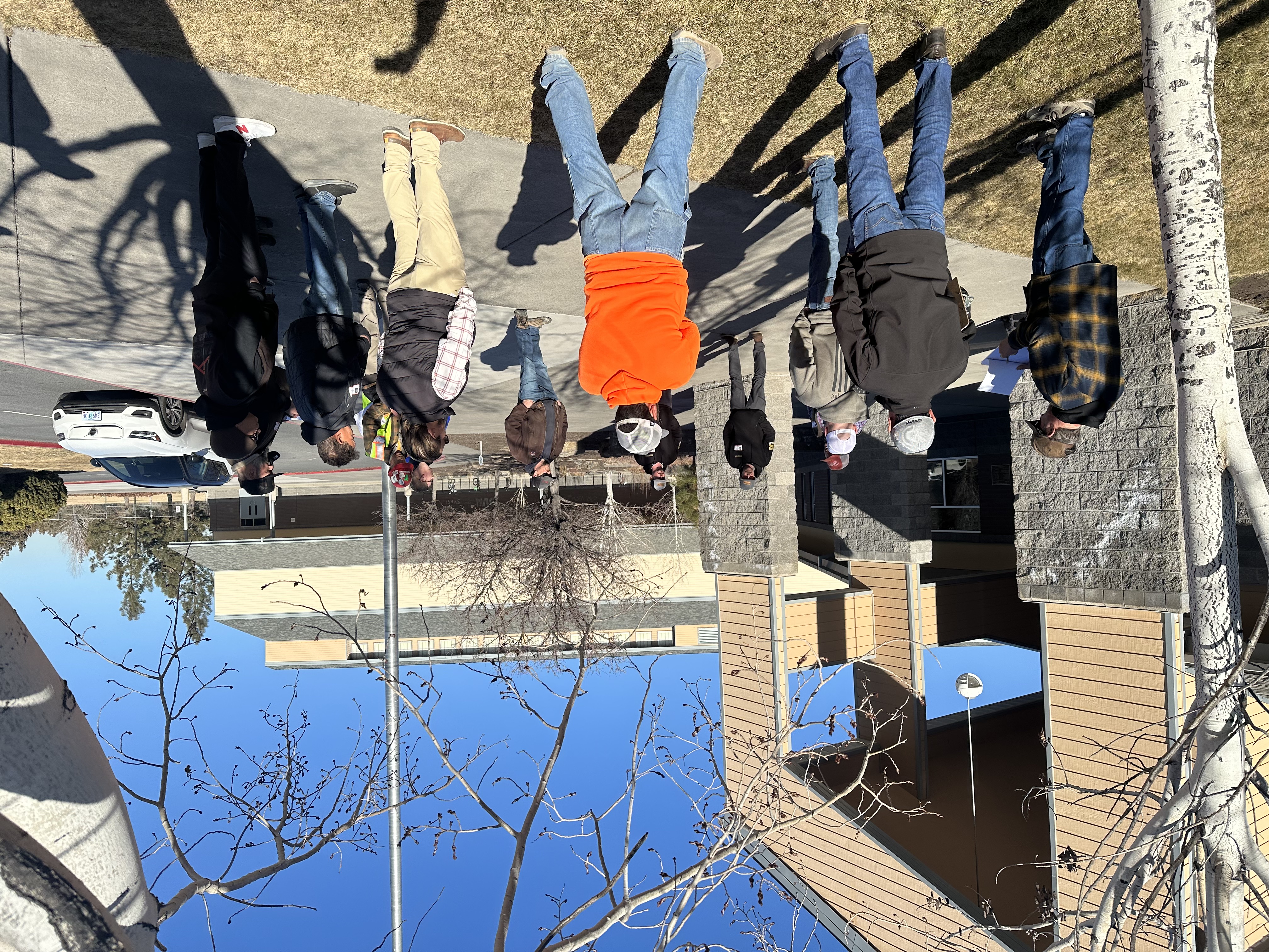 ten people stand in a circle outside of Sky View Middle School entrance on sunny day
