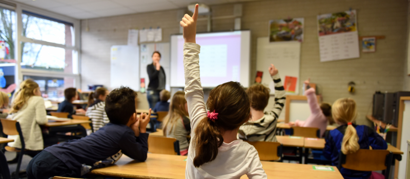 back of middle school classroom with girl standing up with hand up